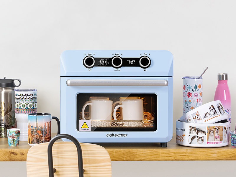 Craft Express sublimation oven with mugs inside on table with products